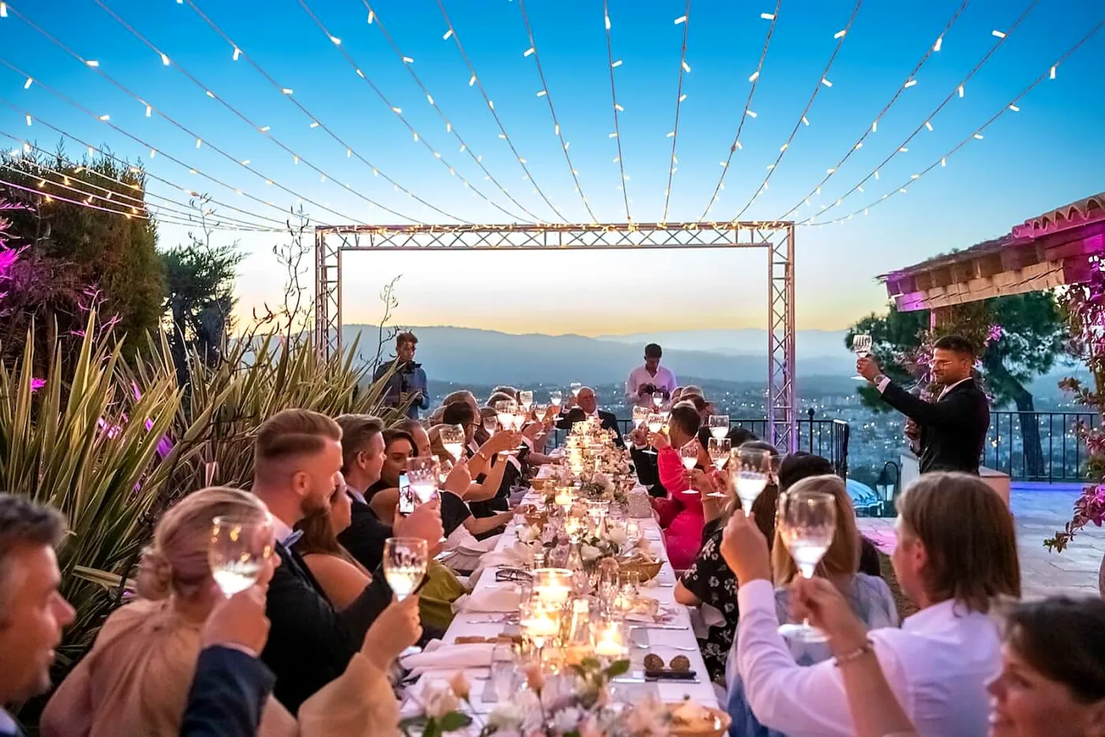 Invités réunis autour d’une longue table en extérieur, sous des guirlandes lumineuses